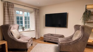 A living room with two armchairs, a coffee table, a flat-screen TV, and a window with curtains.