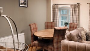 A dining area with a round table, plaid chairs, a wicker chair, a sofa, and a window with curtains.
