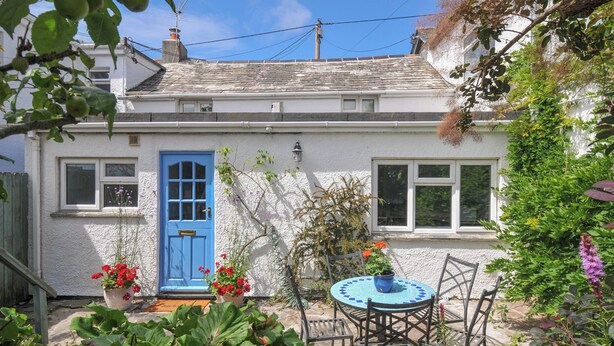 A quaint house with a blue door, a small garden with a round table and chairs, and a white exterior. - 2 Porthilly Cottages (Wadebridge)