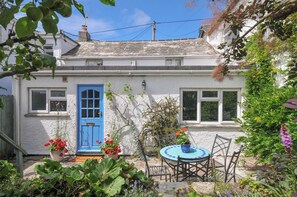 A quaint house with a blue door, a small garden with a round table and chairs, and a white exterior.