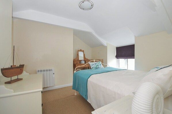 A bedroom with a bed, a dresser, a mirror, a ship decoration, and a window with a view.