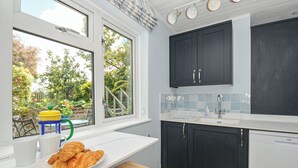 A modern kitchen with a large window, a breakfast setup with croissants, and a view of a garden. - 2 Porthilly Cottages (Wadebridge)
