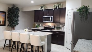 A modern kitchen with dark cabinets, a stainless steel microwave, and a granite countertop. There are four bar stools and a potted plant. - Beautiful and Comfy 4-bedroom house with AC in Maricopa (Maricopa)