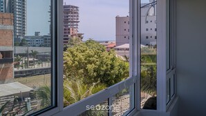 A view from a window overlooking a cityscape with various buildings, including a tall structure and a shorter building with a red roof. - Charming Apt 550m From Pereque Beach - Rne0301 (Porto Belo)
