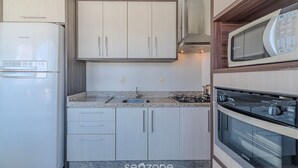 A compact kitchen with a built-in refrigerator, a microwave, and a stove. There is a sink with a faucet, and cabinets above and below the countertop. - Charming Apt 550m From Pereque Beach - Rne0301 (Porto Belo)