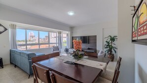 A modern living room with a dining area, large windows, a flat-screen TV, and a potted plant. - Charming Apt 550m From Pereque Beach - Rne0301 (Porto Belo)