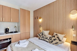 Una habitación de hotel moderna con cama, una kitchenette pequeña y una pared de acento de madera.