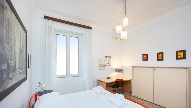 A hotel room with a bed, desk, wardrobe, and artwork on the walls. - Rental in Rome Clodia 5 Apartment (Rome)
