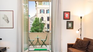 A modern living room with a glass door leading to a balcony, a brown sofa, a small table, and framed pictures on the wall. - Rental in Rome Clodia 5 Apartment (Rome)