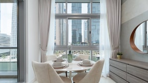 Un coin repas avec une table dressée pour deux personnes, une vue sur de hauts immeubles et une grande fenêtre avec des rideaux.