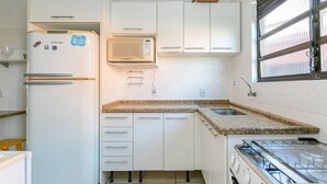 A compact kitchen with white cabinetry, a built-in microwave, a gas stove, and a window with blinds.