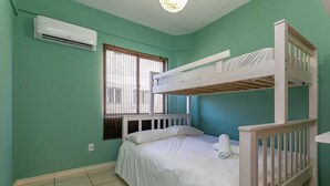 A bunk bed room with a window, an air conditioning unit, and a tiled floor.