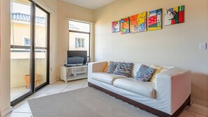 A living room with a sofa, a TV on a stand, and a balcony with a sliding door.