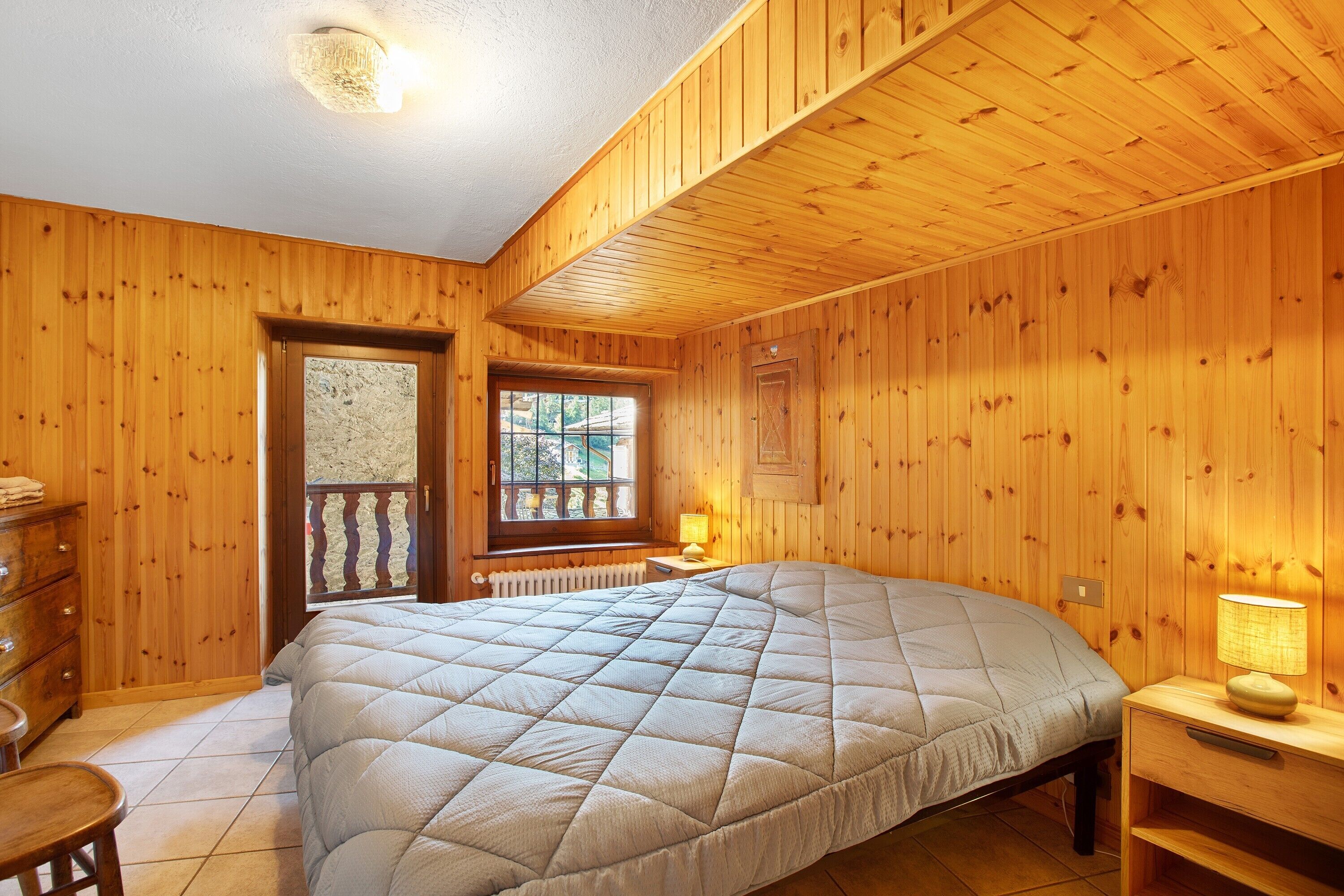 A wooden-paneled room with a bed, a dresser, a window, and a lamp.