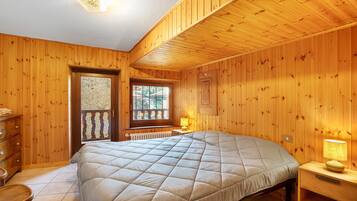 A wooden-paneled room with a bed, a dresser, a window, and a lamp.