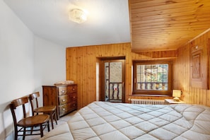 Une chambre à coucher avec un lit, des murs en bois, une commode, des chaises, une fenêtre donnant sur un paysage agréable et un radiateur.
