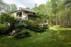 Une maison moderne dotée d’une grande fenêtre, d’un escalier et d’un jardin bien entretenu.
