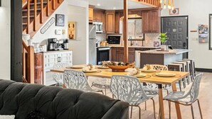Une cuisine moderne avec des meubles en bois, un coin repas avec une table dressée pour quatre personnes, et un escalier menant à l’étage supérieur.