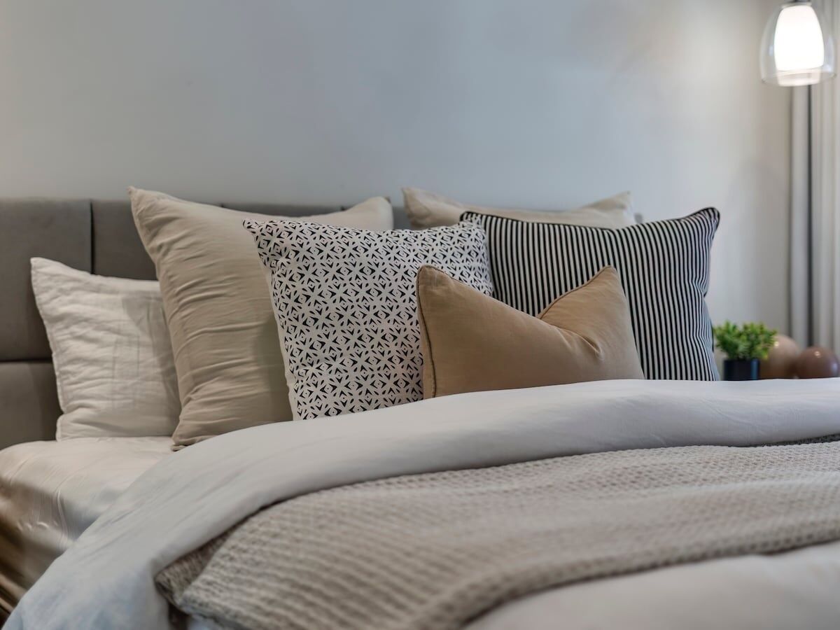 Ein ordentlich bezogenes Bett mit verschiedenen Kissen und einer gemusterten Decke.