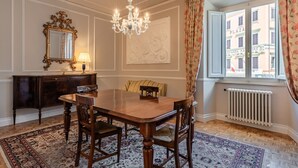 Ein Esszimmer mit Holztisch, Stühlen, einer Kandelaber, einem Spiegel und Blick auf ein Gebäude durch ein Fenster.