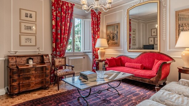 Ein Zimmer mit einem roten Sofa, einem hölzernen Schminktisch, einem Glastisch und einem großen Spiegel.