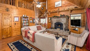 L’intérieur d’un chalet confortable, avec une cheminée, un ventilateur de plafond, une bibliothèque et un téléviseur.