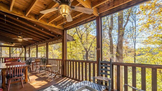 Une terrasse en bois avec une table et des chaises, de grandes fenêtres et un ventilateur de plafond.