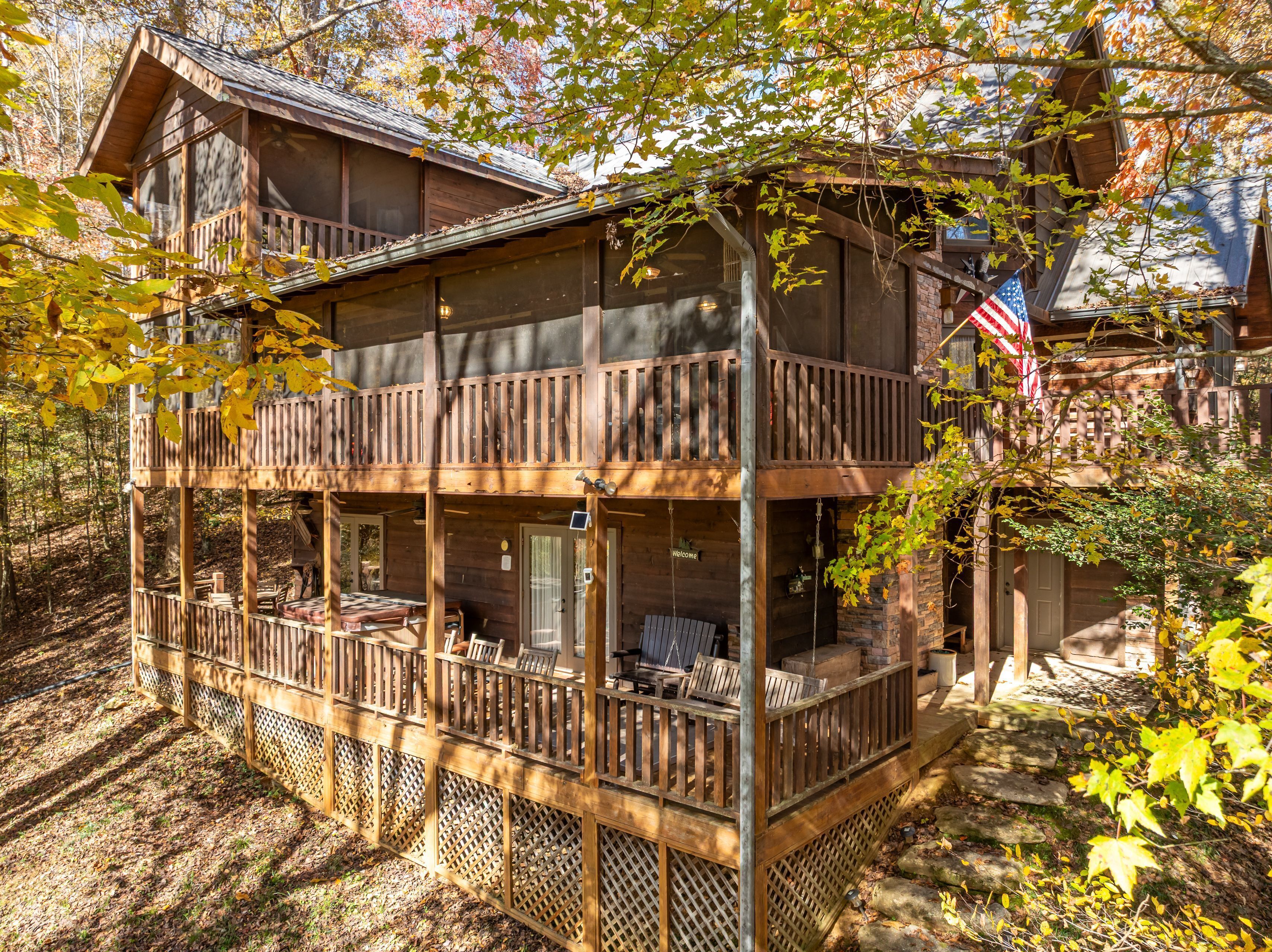 Une cabane en bois à deux étages, dotée d’un balcon, entourée d’arbres et agrémentée d’une terrasse en bois.