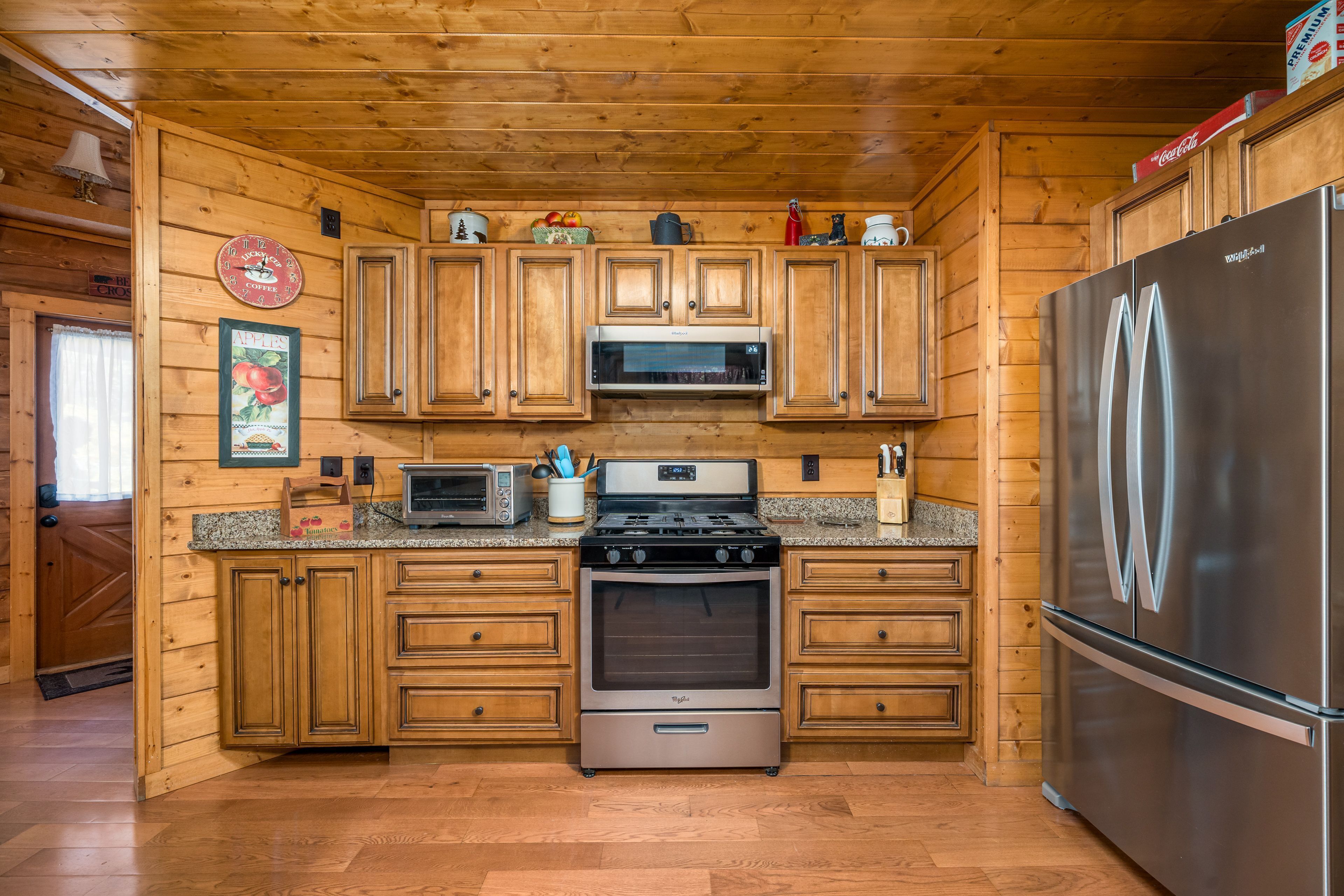 A wooden cabin-style kitchen with a stainless steel refrigerator, a microwave, a stove, and wooden cabinets.