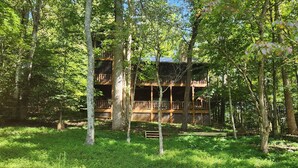 Une cabane en bois dotée d’une terrasse, entourée d’arbres, avec un foyer au premier plan.