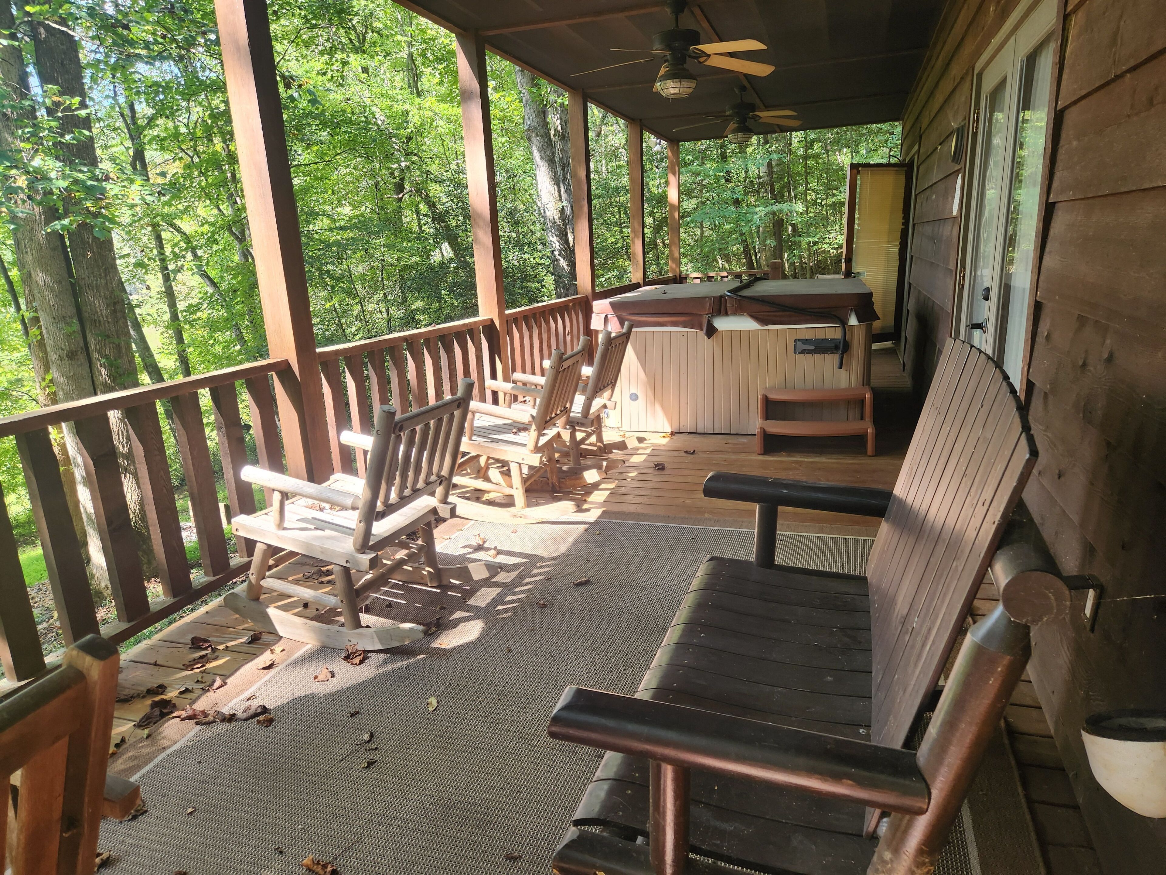 A wooden deck with outdoor seating, a ceiling fan, and a view of a forested area.