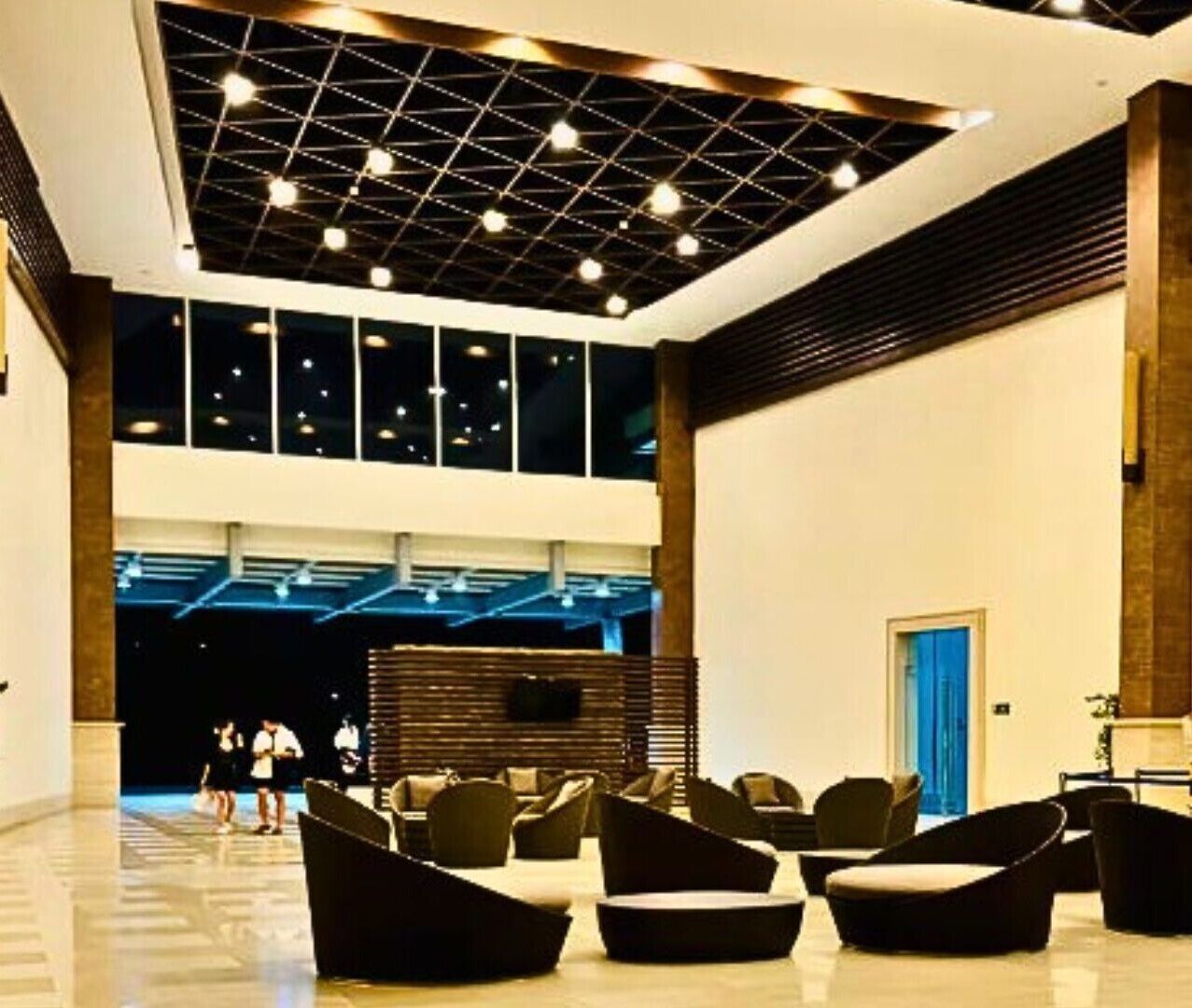 A spacious lobby with modern seating, a high ceiling with lighting fixtures, and large windows.