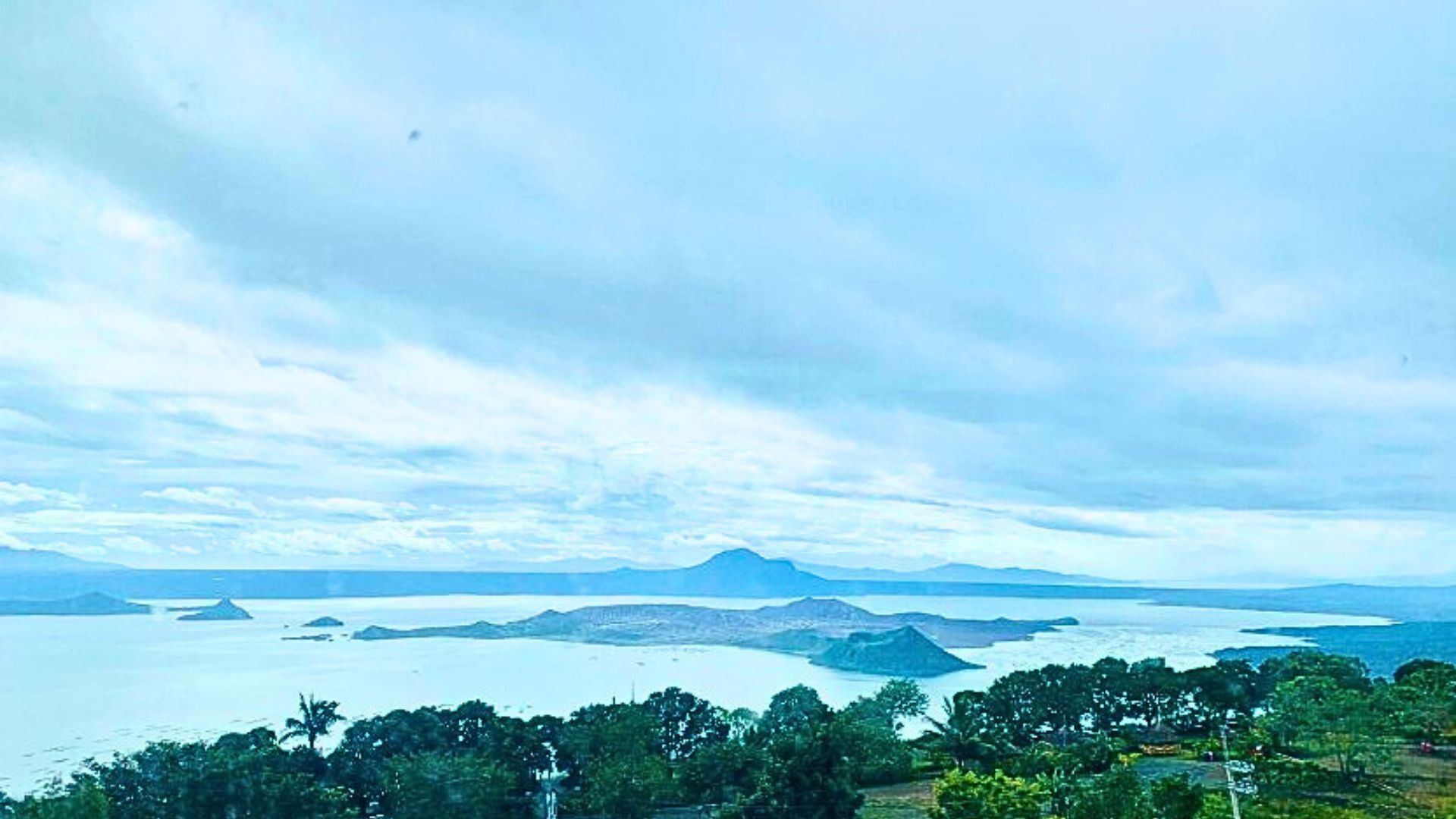 A coastal landscape with a view of the sea, distant mountains, and a forested area.