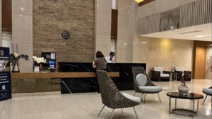 Eine moderne Hotelhalle mit einer Rezeption, einer Sitzecke und einer hohen Decke mit Holzvertäfelung.
