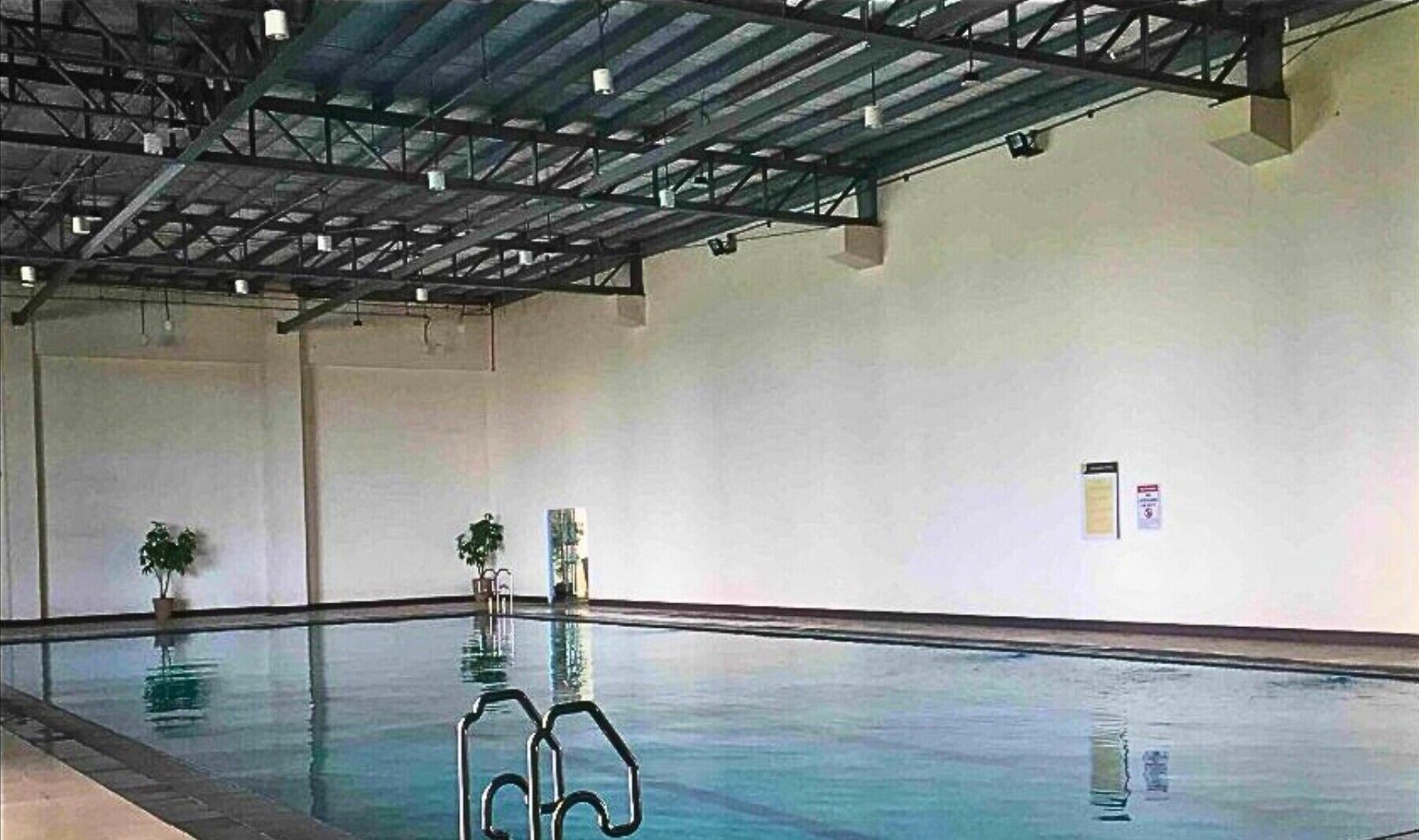 An indoor swimming pool with clear water, metal railings, and potted plants.