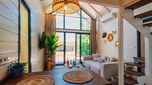 Un interior acogedor con una mesa de comedor de madera, individuales tejidos, una lámpara colgante y una escalera que lleva a un nivel superior.