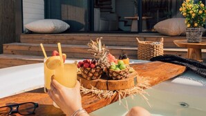 Una persona relajándose en un jacuzzi con una cesta de frutas y una bebida.