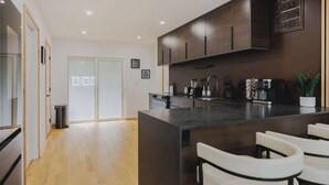 Une cuisine moderne avec des meubles de couleur sombre, un îlot central et des sièges de style bar.