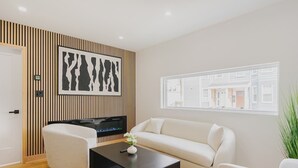 Un salon moderne doté d’un téléviseur à écran plat, d’un canapé blanc, d’une table basse noire et d’une grande fenêtre offrant une vue sur les immebles.