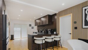 Une cuisine moderne avec un îlot central, des tabourets de bar et un canapé blanc dans un espace de vie lumineux.
