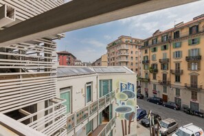 A multi-story building with balconies, a street view, and parked cars.