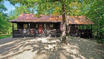 A rustic cabin with a metal roof, wooden deck, and an American flag.