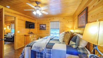 A cozy cabin room with a bed, a ceiling fan, a TV, and a window.