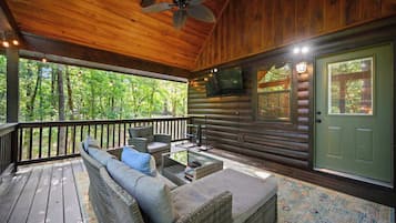 A covered porch with wicker furniture, a television, and a green door.