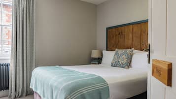 A neatly made bed with a patterned blanket, a bedside table with a lamp, and a wooden door with a nameplate.