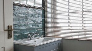 A bathroom with a sink, a mirror, and a window with blinds. - The Bear Hotel (Wareham)