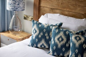 A neatly made bed with white linens and two patterned pillows, a wooden headboard, and a nightstand with a lamp and a glass container. - The Bear Hotel (Wareham)