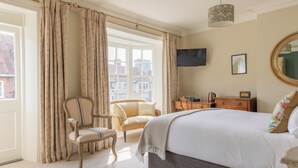 A bedroom with a bed, a chair, a dresser, a television, and a window with curtains. - The Bear Hotel (Wareham)