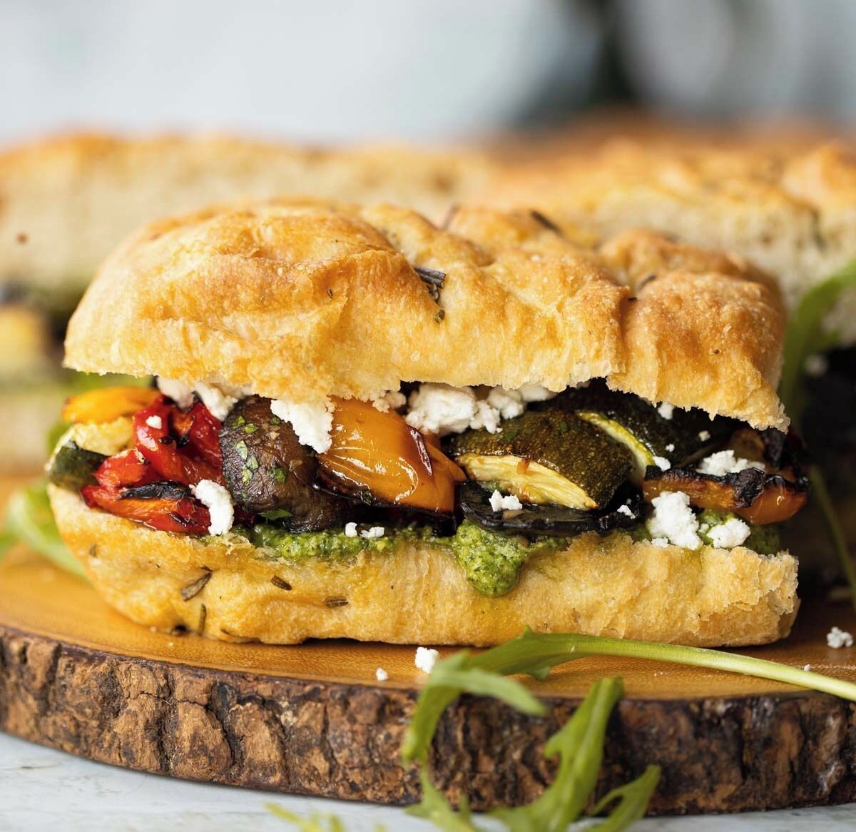 A sandwich with various vegetables and cheese on a wooden board.