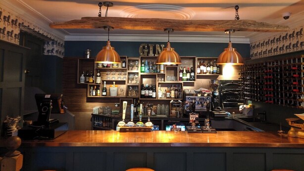 A bar area with wooden shelves stocked with bottles, a bar counter, and three pendant lights. - The Bear Hotel (Wareham)